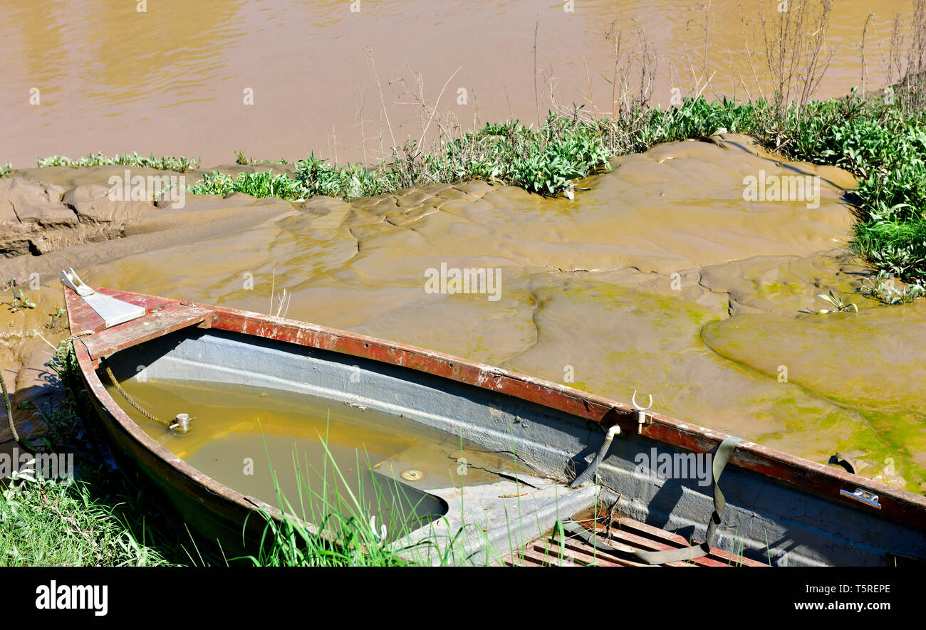 Piccola imbarcazione parzialmente riempita con acqua fango sulla riva del fiume Foto Stock