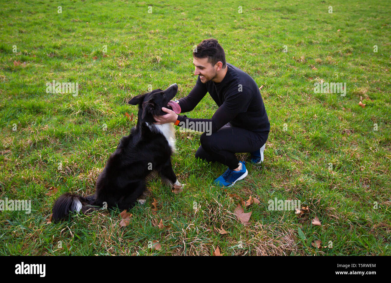 Uomo cane giocare all'aperto nel parco. Giovane proprietario avvolge il suo pet. L'amicizia tra il proprietario e il cane. Amore animale concetto. Foto Stock