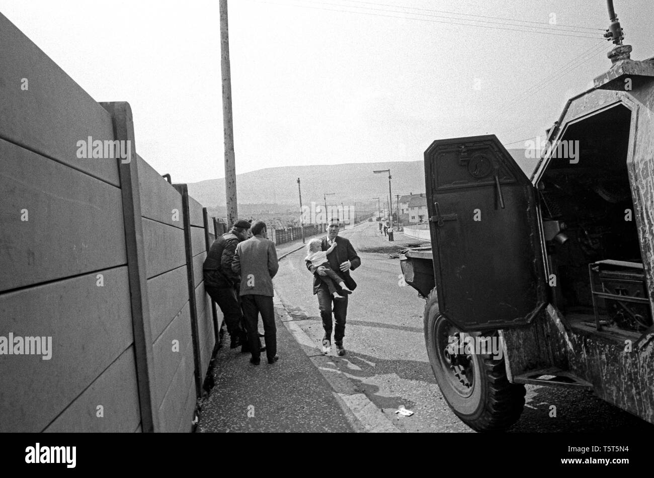 Padre con bambino in esecuzione per coprire durante un'IRA sniper attack, Ballymurphy, parte occidentale di Belfast, Irlanda del Nord nei primi anni settanta durante i guai Foto Stock
