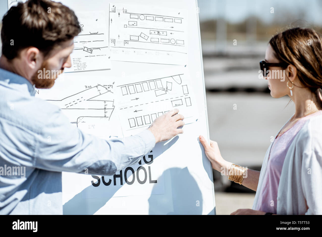 Istruttore di sesso maschile che mostra il traffico shemes ad una giovane studentessa in piedi sul campo di allenamento presso il conducente della scuola Foto Stock