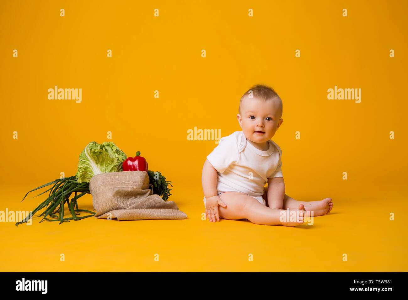 Baby ragazza seduta con la sacca di verdure su giallo isolare lo sfondo, lo spazio per il testo. il concetto di sano cibo eating.organic Foto Stock