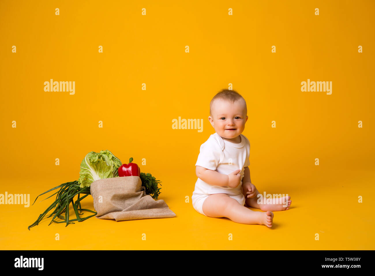 Baby ragazza seduta con la sacca di verdure su giallo isolare lo sfondo, lo spazio per il testo. il concetto di sano cibo eating.organic Foto Stock