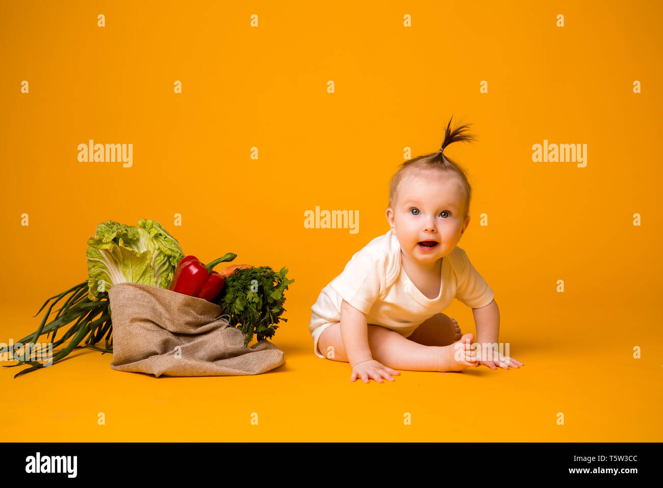 Baby ragazza seduta con la sacca di verdure su giallo isolare lo sfondo, lo spazio per il testo. il concetto di sano cibo eating.organic Foto Stock