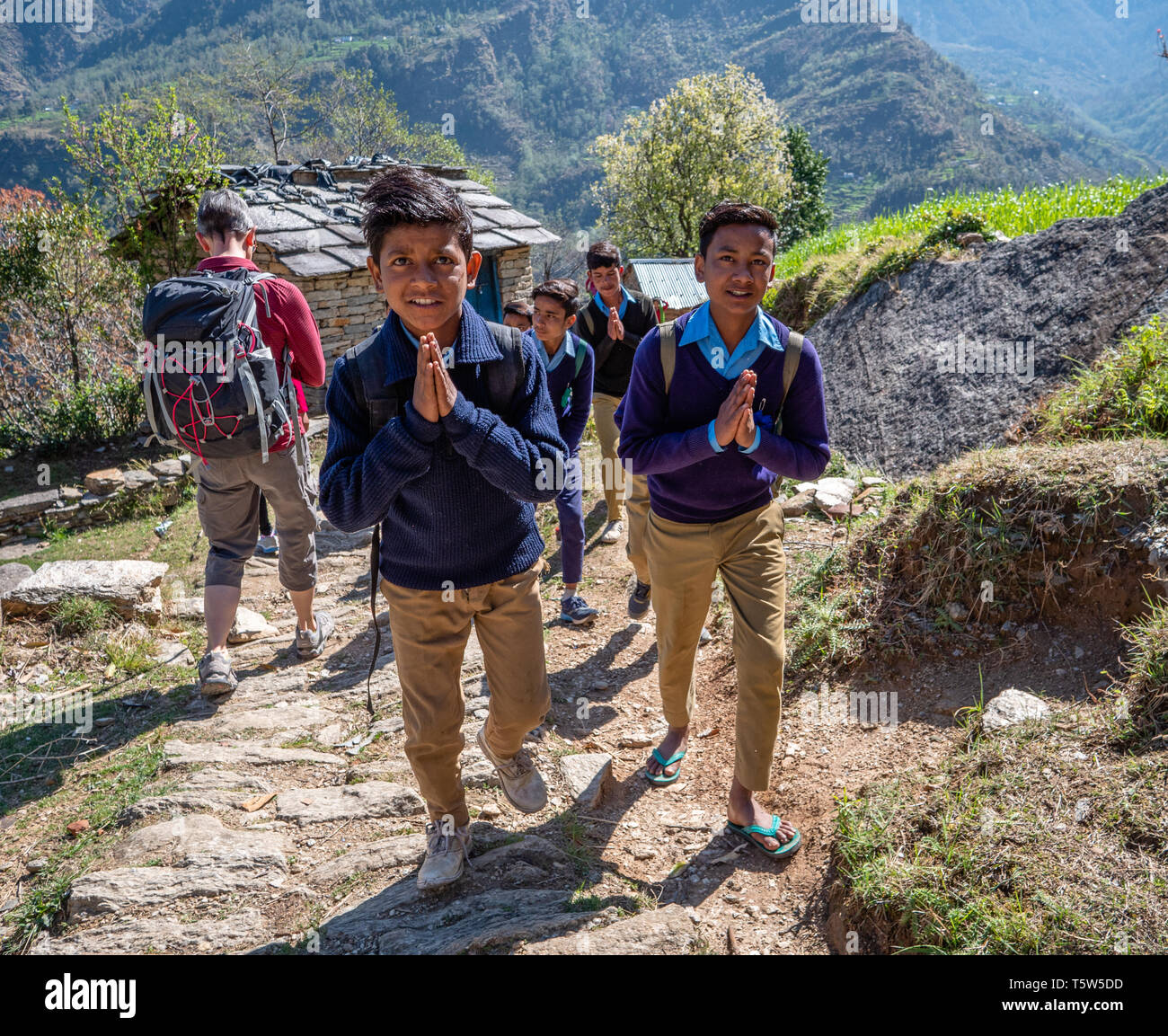 Elegantemente vestito scolari sul loro modo di scuola dando un educato ed orante Namaste per passare i visitatori nel villaggio Supi Uttarakhand India del Nord Foto Stock
