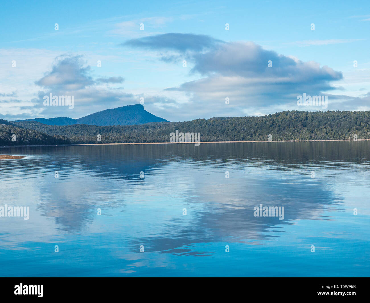 Nuvole e cielo blu riflessa in acqua calma, lontane colline, una giornata autunnale al Lago Hauroko, Parco Nazionale di Fiordland, Southland, Nuova Zelanda Foto Stock