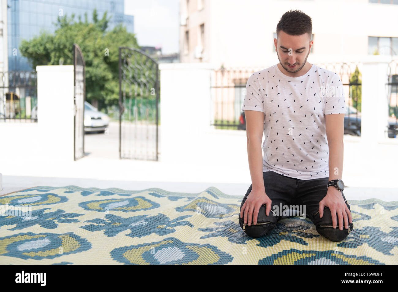 Uomo musulmano rendendo tradizionale preghiera a Dio Allah all'aperto davanti alla moschea Foto Stock
