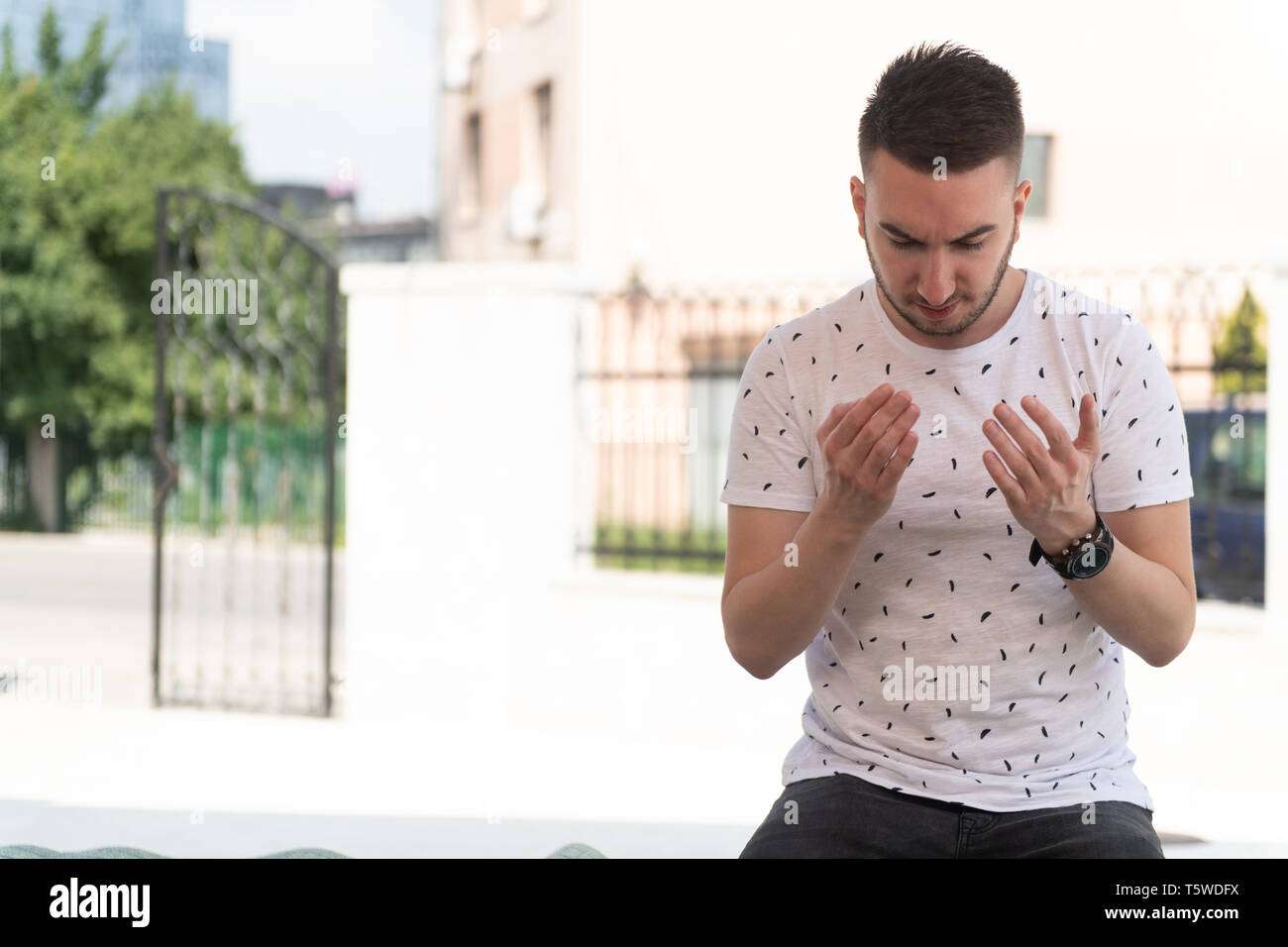 Uomo musulmano rendendo tradizionale preghiera a Dio Allah all'aperto davanti alla moschea Foto Stock