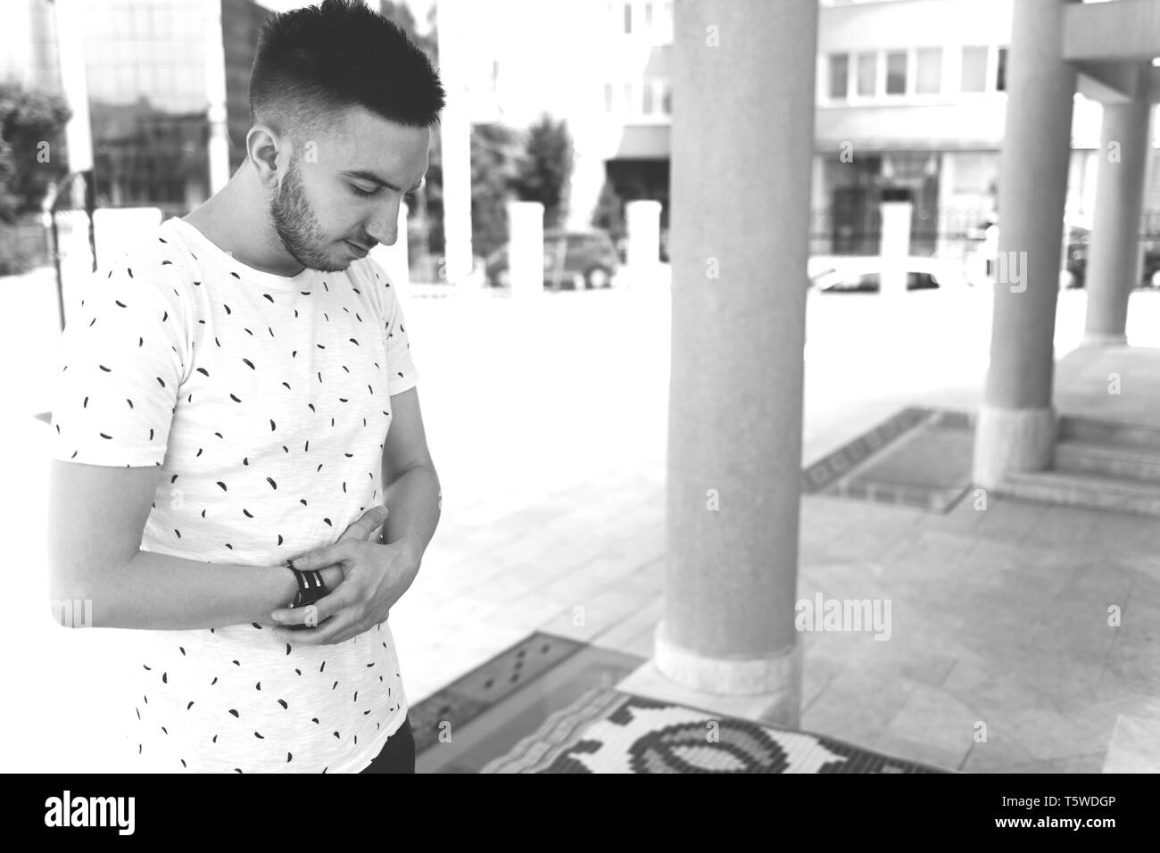 Attraente uomo rendendo tradizionale preghiera a Dio Allah all'aperto davanti alla moschea Foto Stock