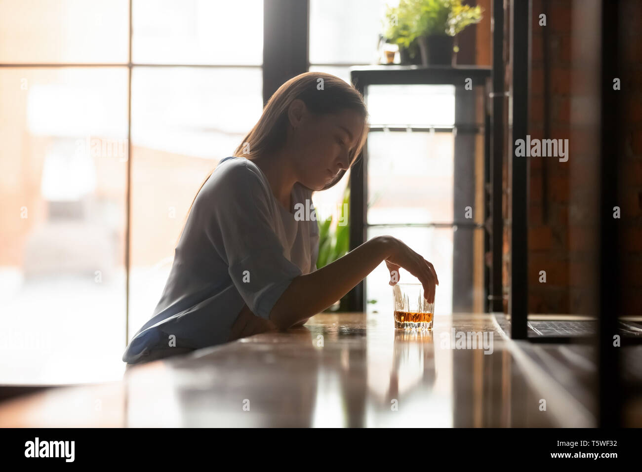 Triste giovane donna seduta sul banco bar a bere alcolici Foto Stock