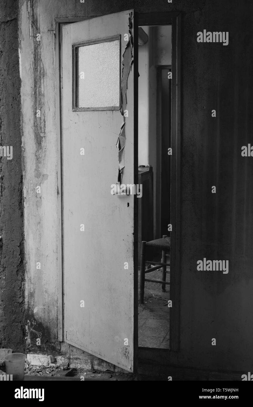 Aperto a metà scricchiolio porta che conduce dalla cucina al corridoio nella vecchia casa abbandonata interni. In bianco e nero. Foto Stock