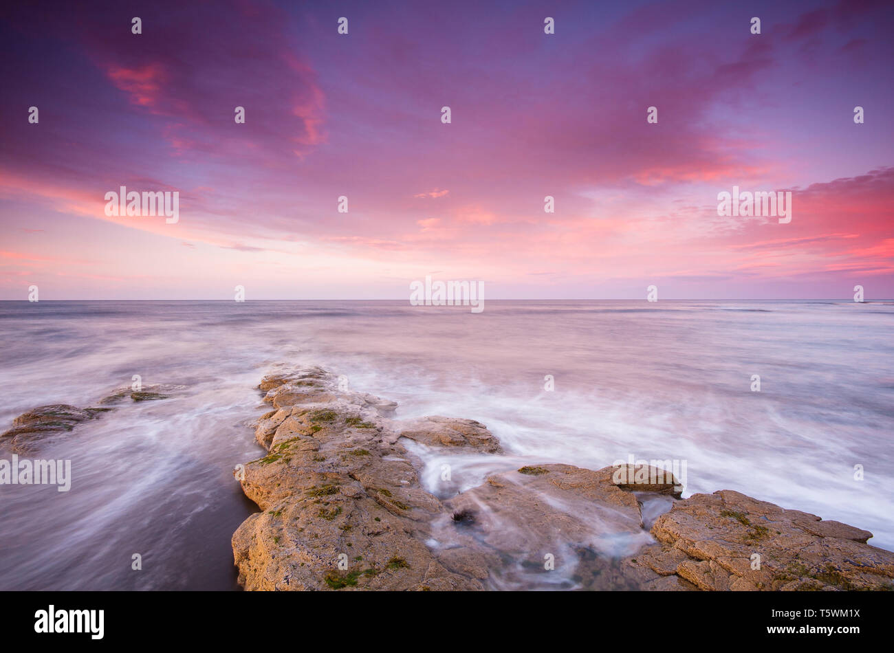 Tramonto sulla spiaggia Cresswell & Northumberland costa guardando fuori nel mare del Nord che è la creazione di moto & riflessioni lungo le rocce. Foto Stock