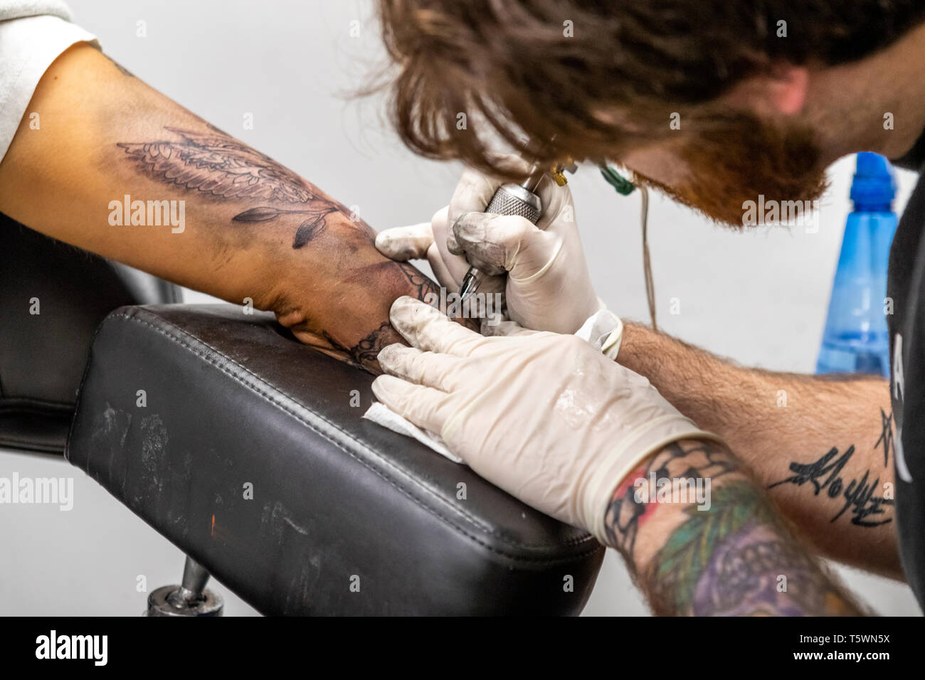Una giovane donna siede mentre un tattooist lavora sull'aggiunta di un design per il suo "sleeve". Chepstow street e persone Foto Stock