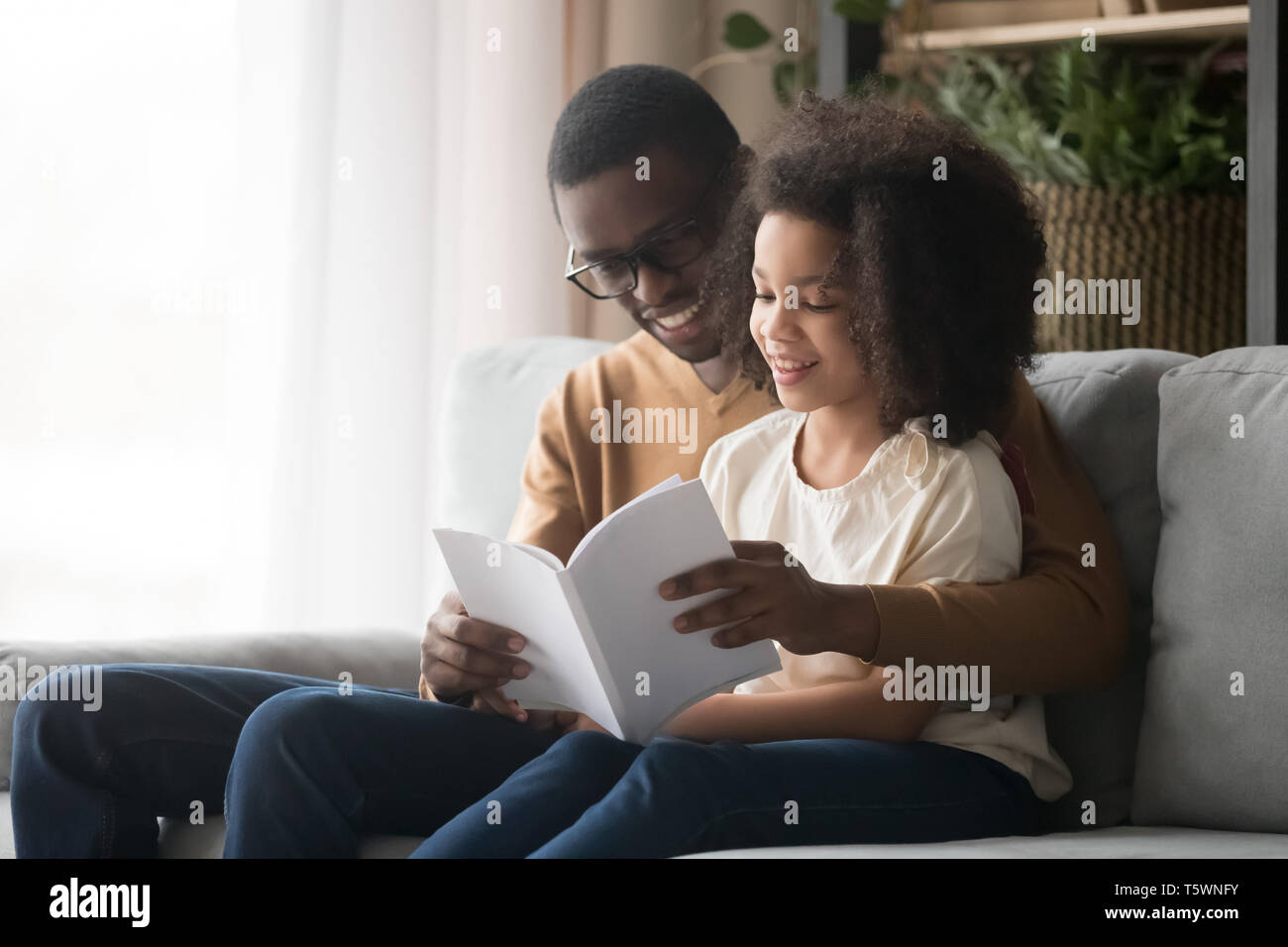Padre nero libro di lettura alla figlia seduta sul lettino Foto Stock