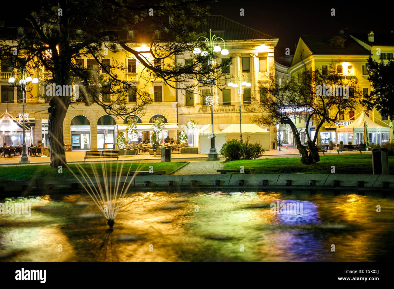 Vista colorate per un enorme fontana con decorazioni antiche e alcuni edifici in background in un villaggio italiano di notte Foto Stock