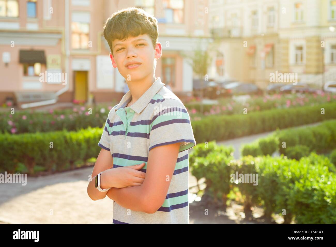 Outdoor ritratto di adolescente di 13, 14 anni, ragazzo con bracci incrociati, background urbano. Foto Stock