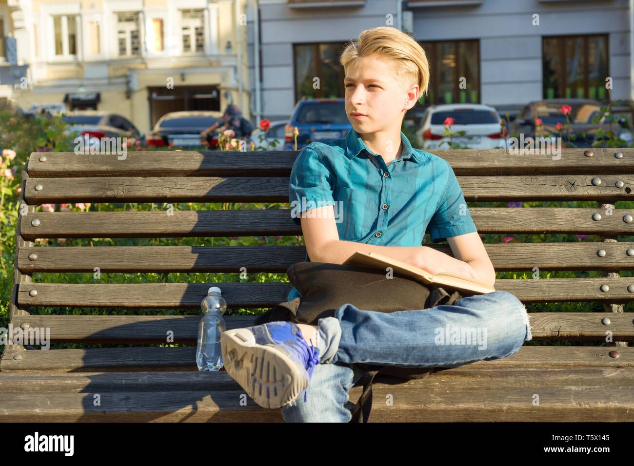 Outdoor ritratto di ragazzo adolescente di 13, 14 anni seduto sulla panchina nel parco della città Foto Stock