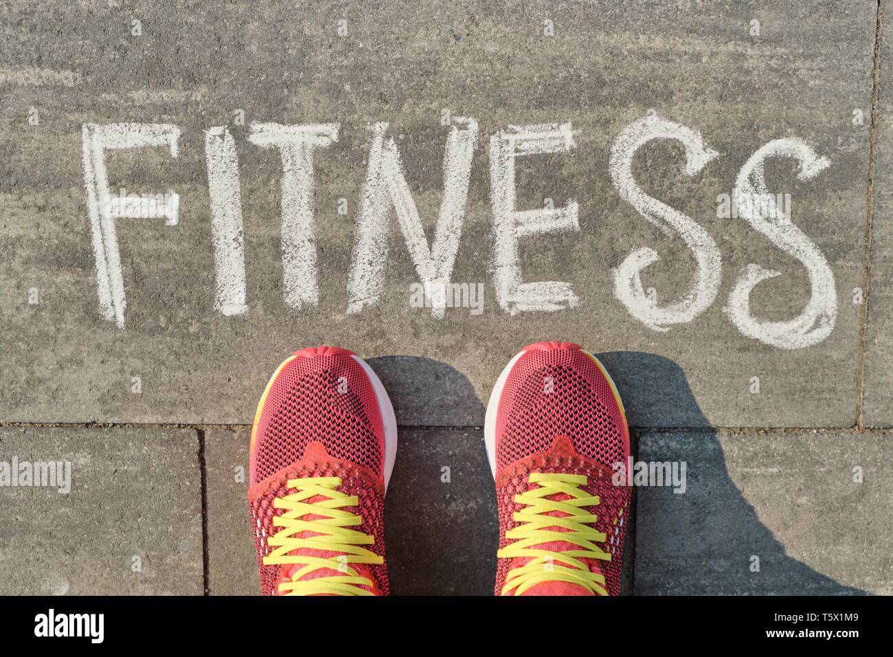 La parola scritta fitness sul marciapiede grigio con gambe di donna in sneakers, vista da sopra. Foto Stock