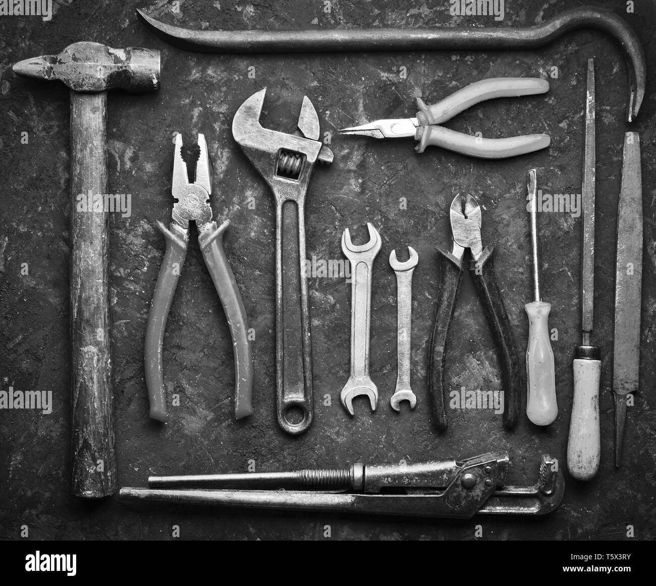 Molti strumenti di lavoro su un calcestruzzo nero tabella. Tronchese, file, pinze, rottami, martello, chiave, cacciavite. Vista dall'alto. Lay piatto. Foto Stock