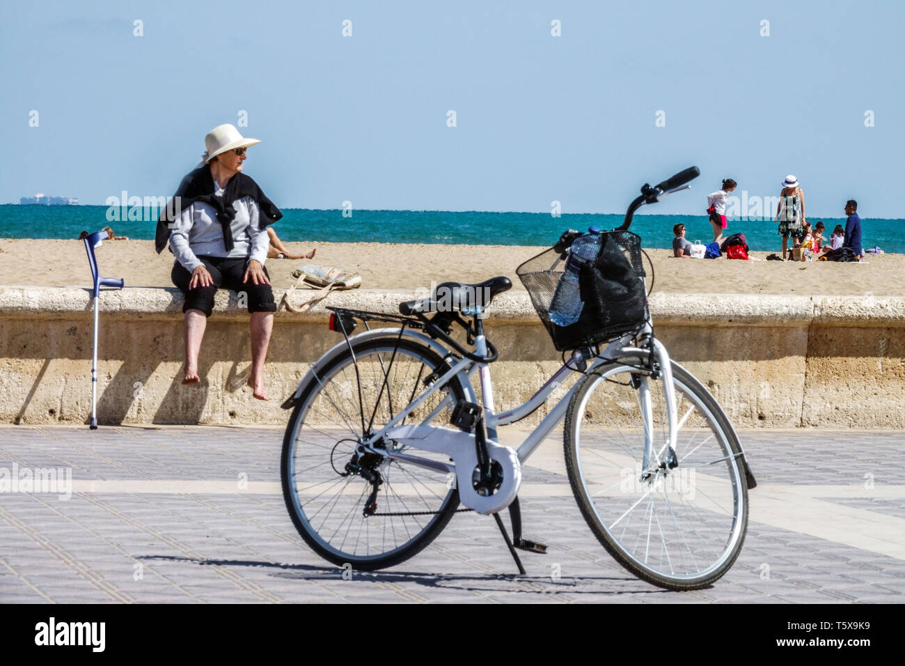 Valencia Malvarrosa Beach turista, donna anziana, bicicletta e gruppo di persone in background sulla spiaggia di sabbia, Spagna Europa vista mare Foto Stock