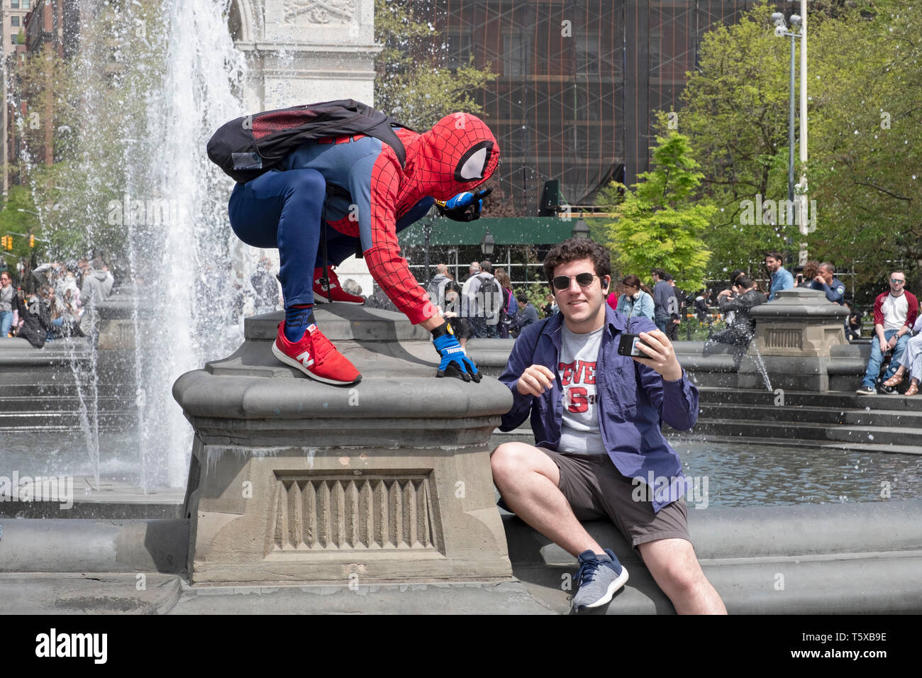 Un giovane uomo di Washington Square Park prendendo un selfie con una performance di artista vestito in un costume di Spiderman. Nella città di New York. Foto Stock