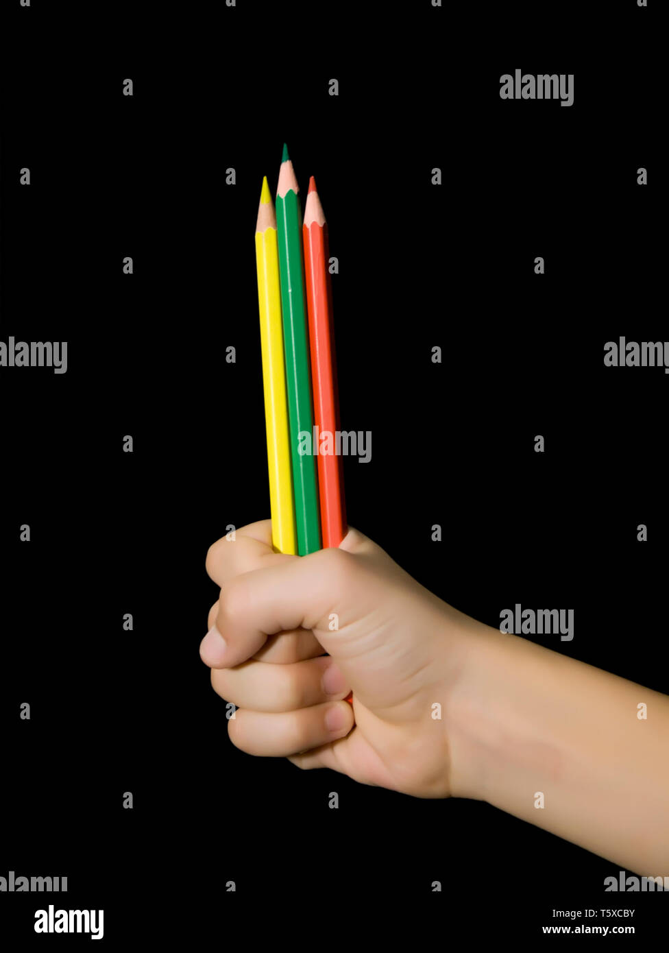 I bambini la mano con tre matite di colore. Giallo, verde e rosso. Sfondo nero Foto Stock