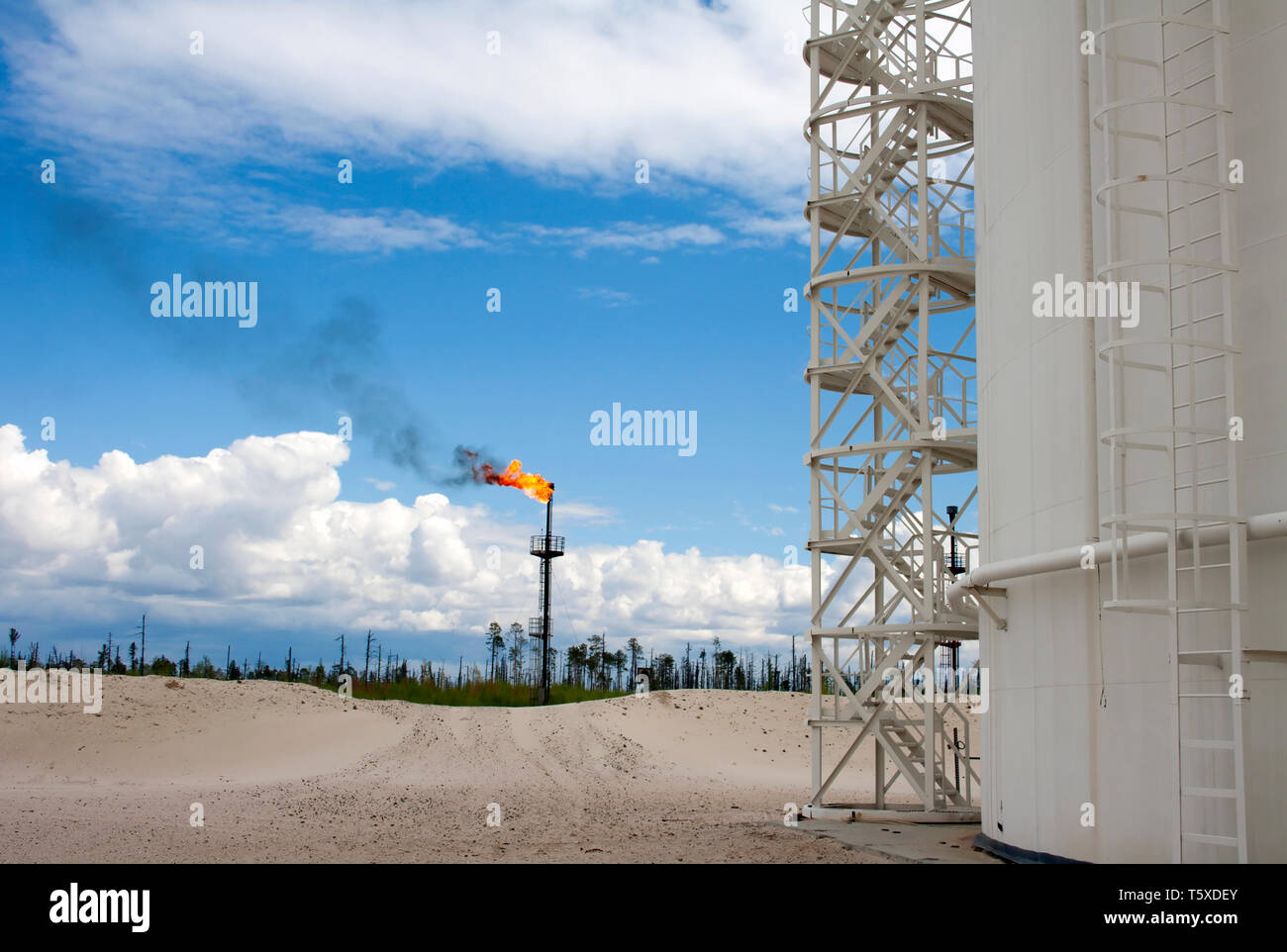 Industria petrolifera. Il gas. Serbatoio olio e torcia a fiamma. Cielo blu e nuvole bianche Foto Stock