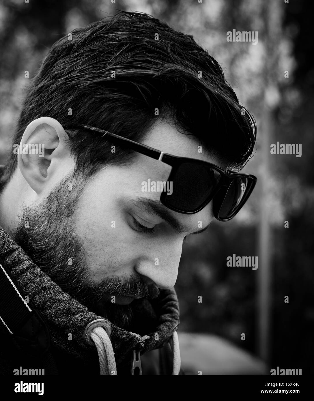 Giovani attraenti uomo barbuto con i capelli scuri e un maglione nel parco con occhiali da sole Foto Stock