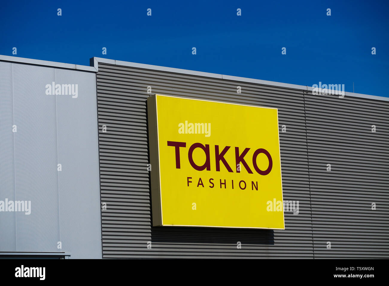 TOENISVORST, Germania - marzo 22. 2019: logo giallo di Takko Fashion(Tedesco della catena di moda) su una facciata contro il cielo blu chiaro Foto Stock