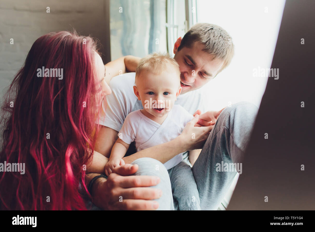 La famiglia felice della madre, padre e figlio figlio di giocare e coccole a casa sul pavimento vicino a una grande finestra. Foto Stock