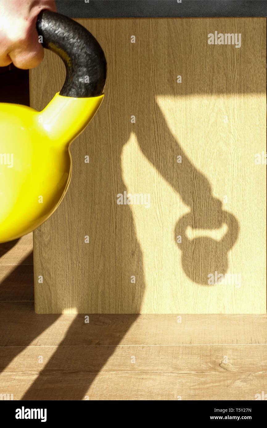 Un maschio di lavorare da casa con un kettlebell. Il sole è dietro di lui getta un' ombra. Kettlebells sono un popolare home palestra opzione per il peso della formazione Foto Stock