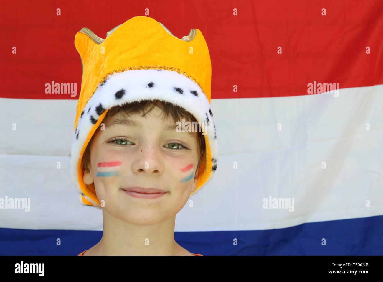 Bambino arancione con la corona in testa davanti a bandiera olandese celebrando il re del giorno Foto Stock