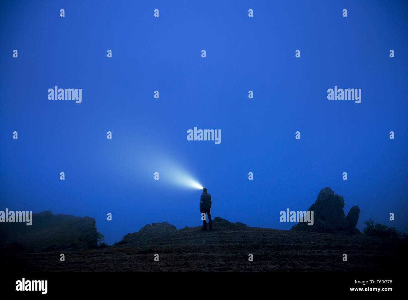 Piccole Silhouette di uomo con proiettore sorge nella nebbia al tramonto Foto Stock