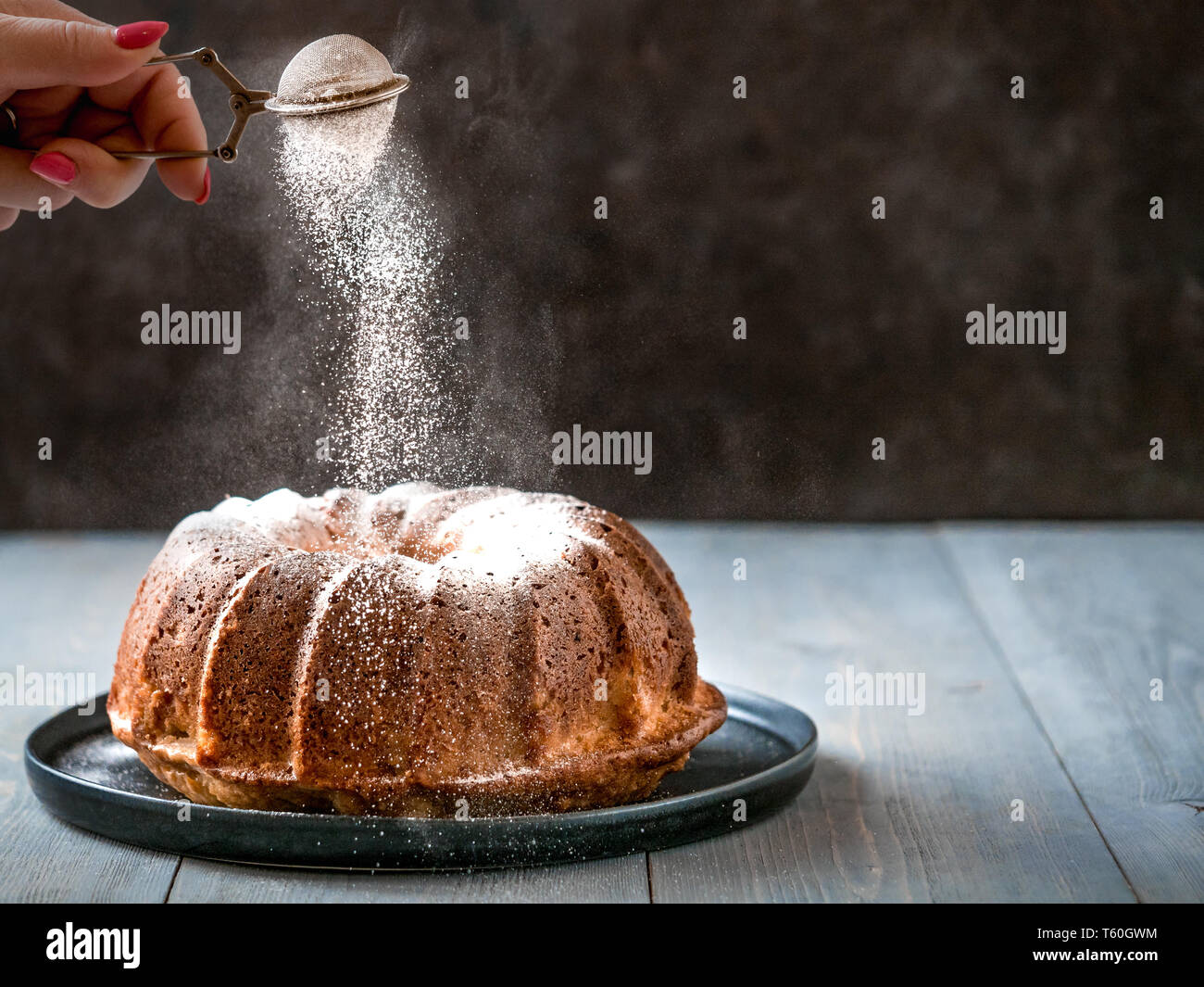 Donna di mano spolverata di zucchero a velo su muffin freschi torta. Lo zucchero in polvere cade su freschi muffin perfetto torta. Copia spazio per il testo. Idee e ricette per la prima colazione o dessert Foto Stock