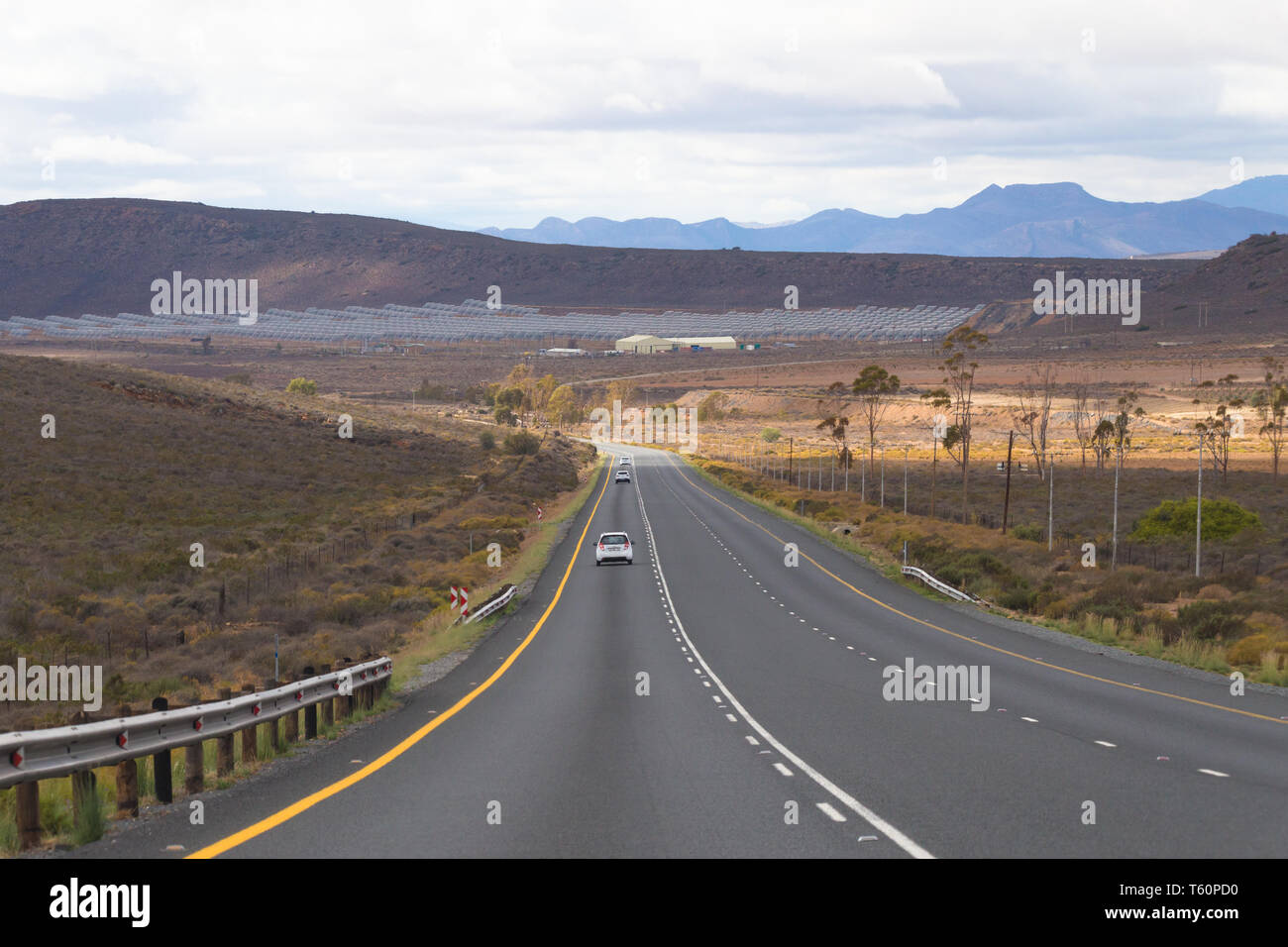 Lungo tratto di asfalto o strada asfaltata in secco e arido deserto semi regione del Karoo in Sud Africa con una energia solare farm su avanti Foto Stock