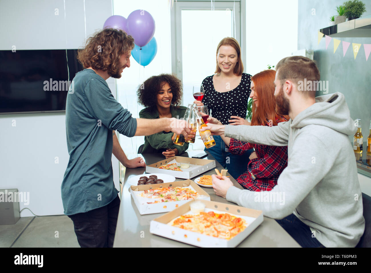 Giovani amici di mangiare pizza e bere birra divertendosi insieme a casa. Foto Stock