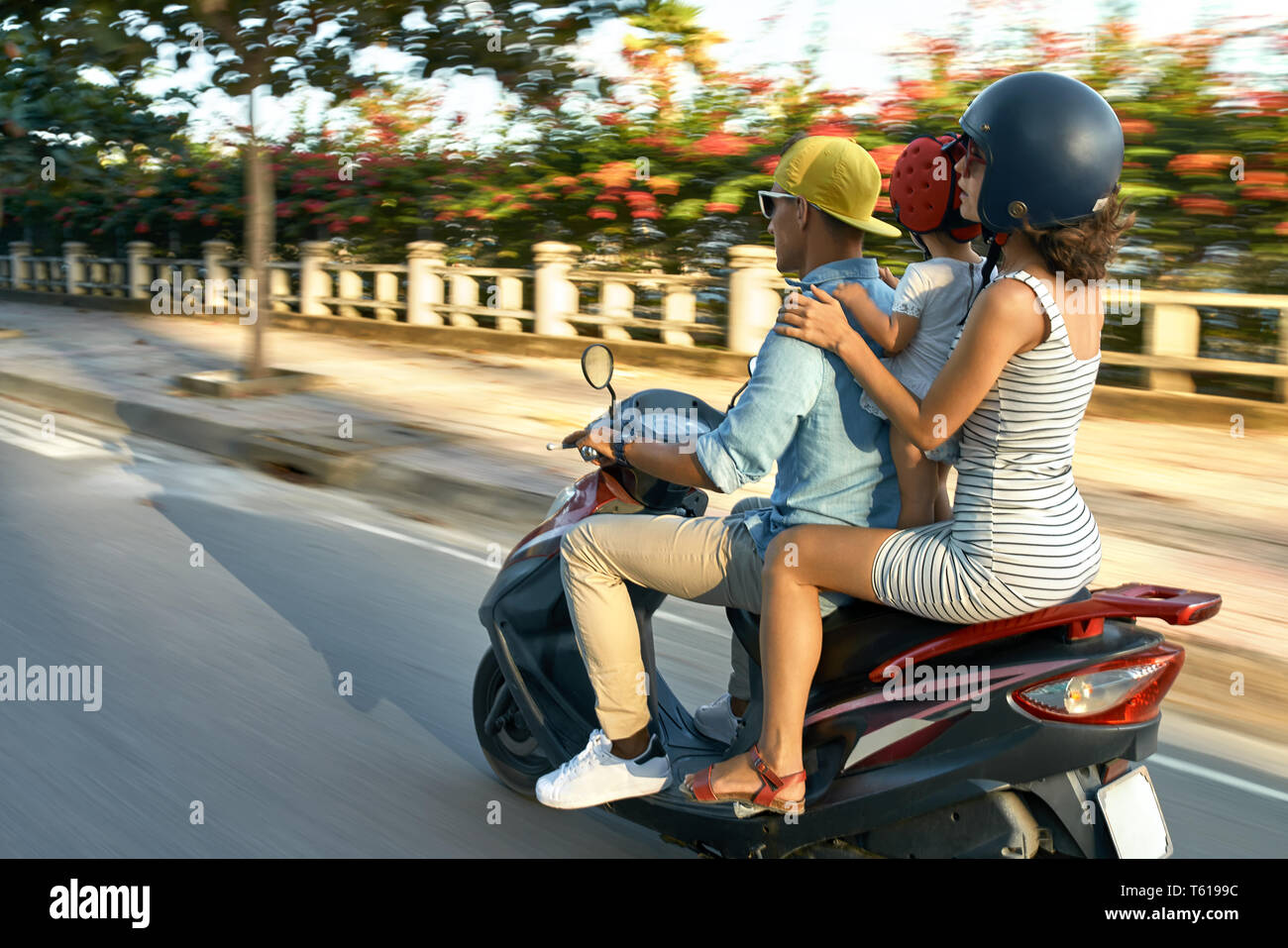 Carino coppia con un bambino piccolo sono rosso di equitazione in moto sulla strada di città sul cielo sereno background in Vietnam. Essi indossano abiti casual, occhiali da sole, Foto Stock