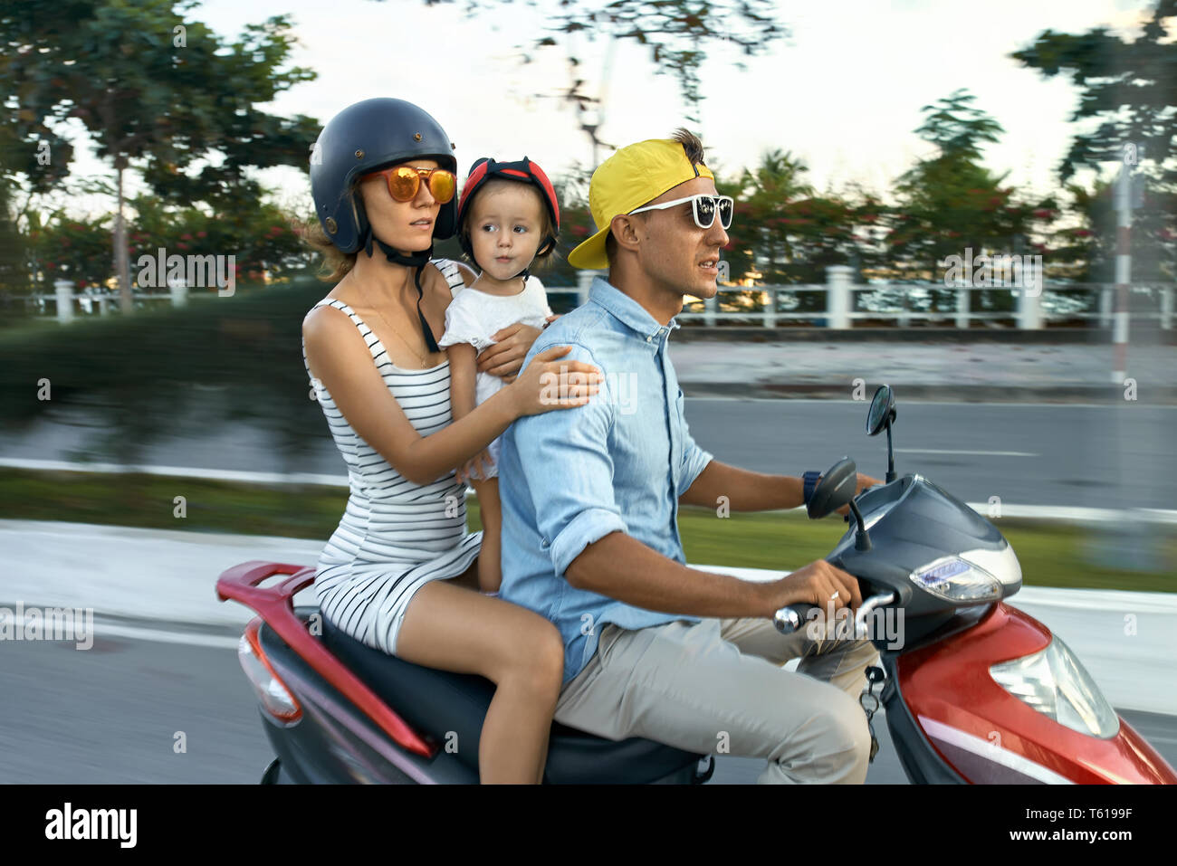 Felice coppia con una piccola figlia di equitazione sono moto rosso sulla strada di città sul cielo sereno background in Vietnam. Essi indossano abiti casual, sunglas Foto Stock