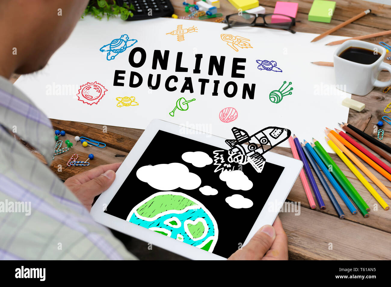 Online il concetto di istruzione con vari disegnati a mano Doodle icone sulla carta. È guardare il tablet con un razzo immagine da schermo e hanno un mondo im Foto Stock