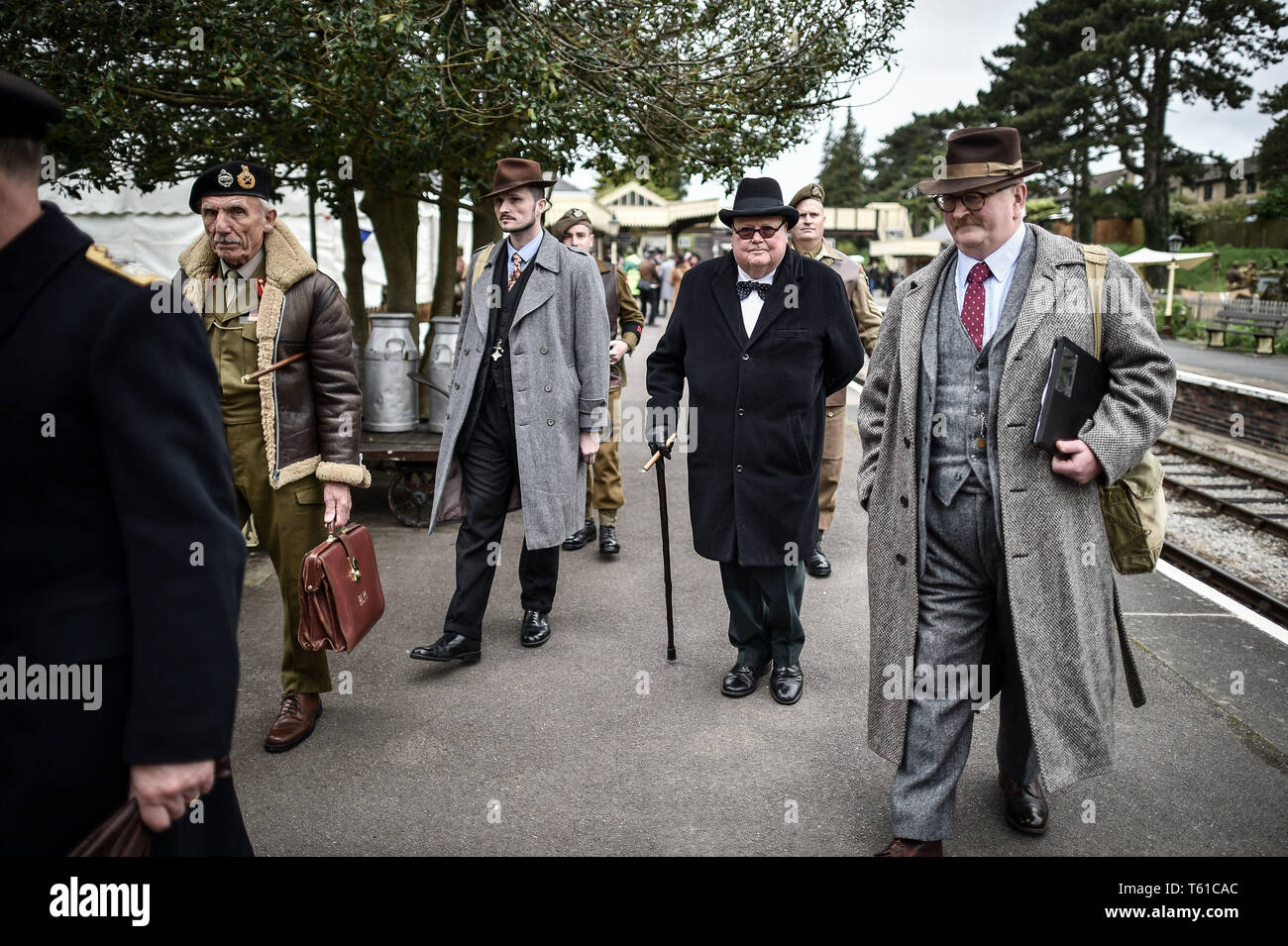 Un uomo vestito come la seconda guerra mondiale il Primo Ministro Winston Churchill passeggiate lungo la piattaforma a Winchcombe affiancato dal suo personale durante il tempo di guerra in Cotswolds evento in Gloucestershire Warwickshire Steam Railway. Foto Stock