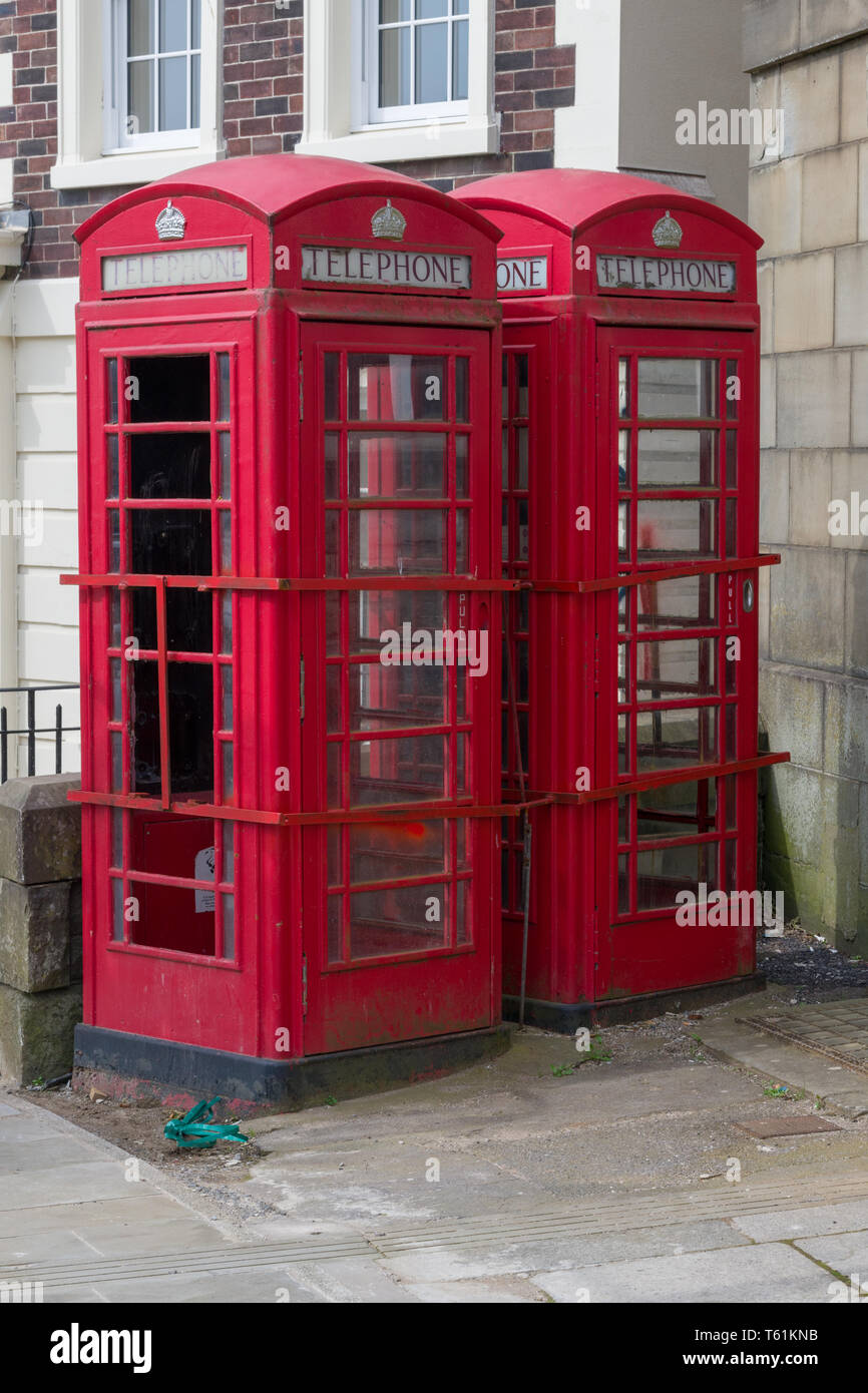 Due cabine telefoniche rosse stand abbandonati e danneggiato in un contesto urbano. Foto Stock