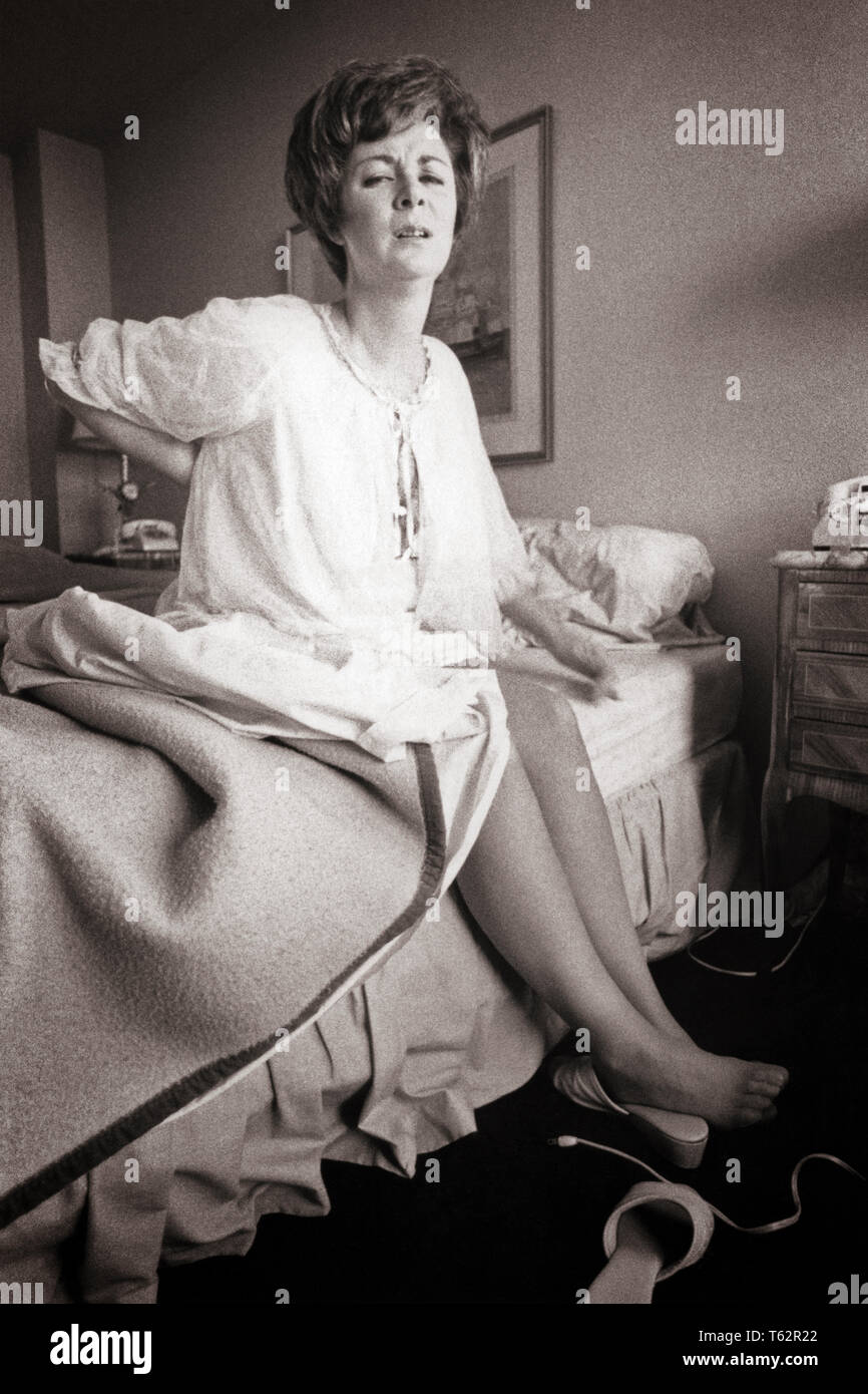 Anni Settanta la donna a scendere dal letto tenendo la schiena con dolorosa espressione facciale - un8365 HAR001 HARS RISVEGLIO ESPRESSIONI AILMENT B&W MATTINA tristezza sofferenza sveglio umore GLUM dolorante di alzarsi di notte abito di cattiva salute malata MID-adulto metà donna adulta miserabile NEGLIGEE doloroso ache in bianco e nero di etnia caucasica HAR001 in vecchio stile Foto Stock