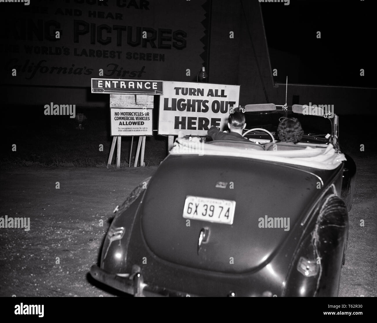 1940s GIOVANE UOMO DONNA IN autovettura convertibile in trazione al drive-in MOVIE THEATER entrata SEGNO - asp ap 8925 Asp001 HARS ragazzo adolescente ENTERTAINMENT B&W FILM DATING sogni entrando in attrazione corteggiamento di fuga di notte Data Motion Pictures possibilità DRIVE IN DRIVE-IN notturno di retrovisione attività sociale Appartenenza giovane uomo adulto giovane donna adulta 1948 in bianco e nero di etnia caucasica il corteggiamento di vecchio stile Foto Stock