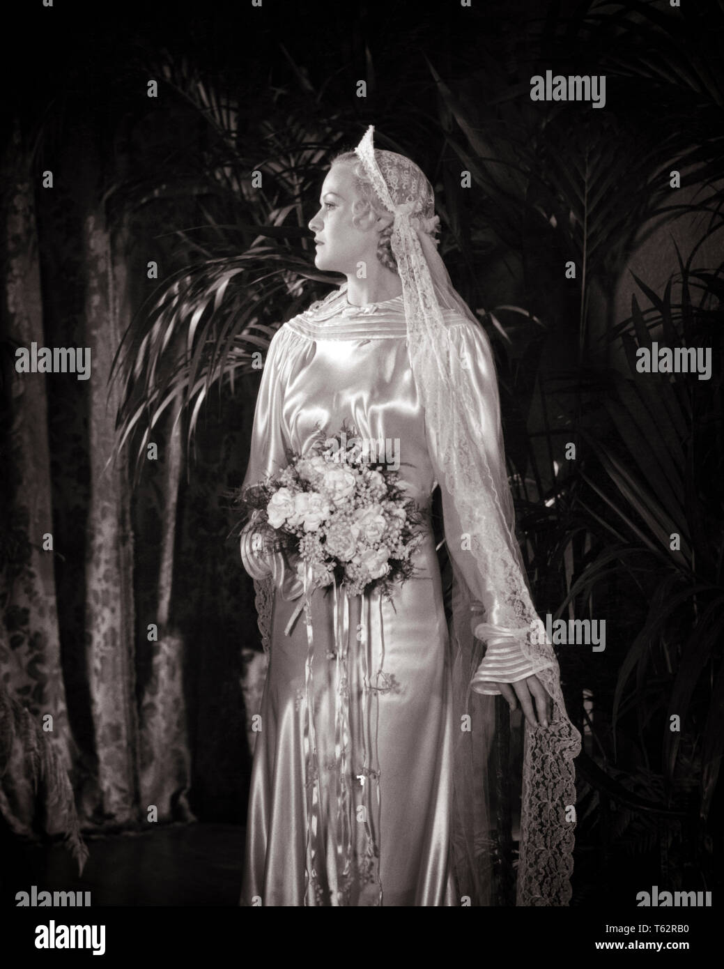 1930 BIONDA sposa nel profilo indossando Abito in raso abito volant nastro collo e polsini testiera con velo bouquet floreali - b14896 HAR001 HARS Evento spazio copia di metà lunghezza LADIES matrimonio persone ispirazione velo satinato fiducia cerimonia B&W nuziale stili di spose personalizzato e tradizione bracciali Nozze Nuziale occasione sposare orgoglio testiera rito di passaggio arruffare elegante MER Mode sposarsi matrimonio giovane donna adulta in bianco e nero di etnia caucasica HAR001 in vecchio stile Foto Stock