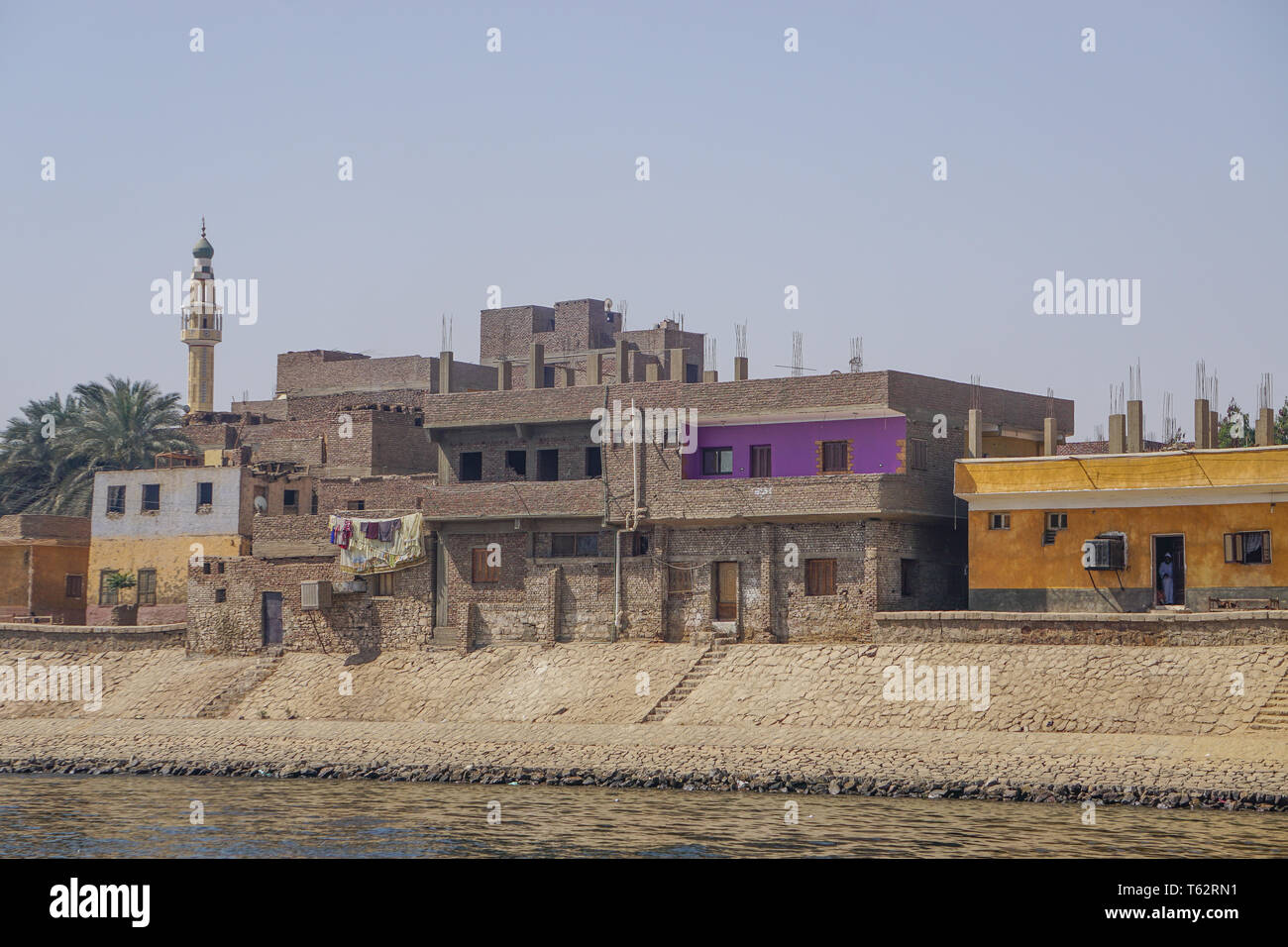 Fiume Nilo in Egitto: case colorate, data di palme, tappeti di essiccazione al sole e un minareto lungo la sponda est del fiume Nilo. Foto Stock