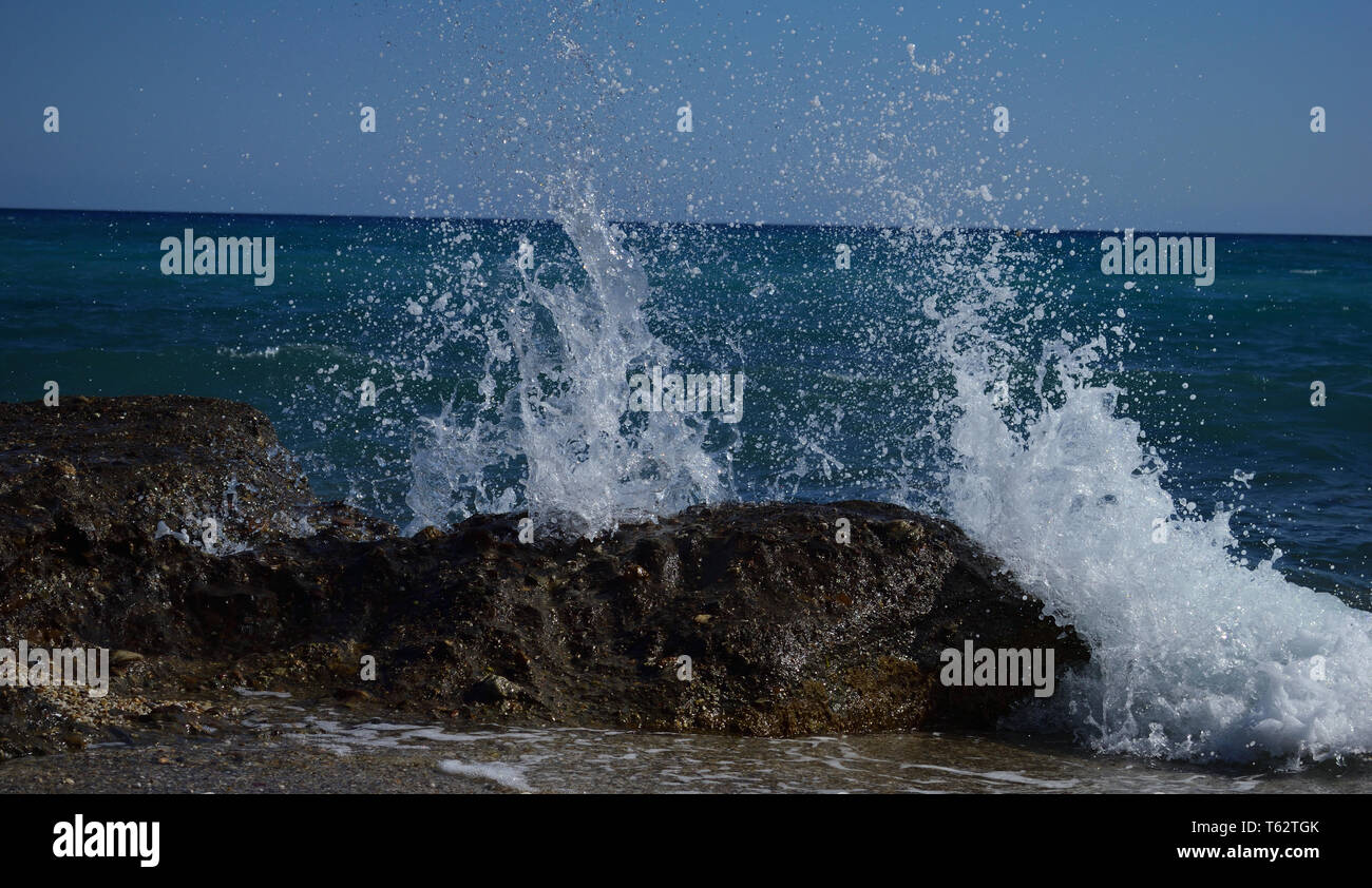 Il mare si schiantava contro le rocce, causando schizzi, su una spiaggia a Mojacar, Spagna meridionale ha preso con una velocità di scatto veloce per catturare l'azione. Foto Stock