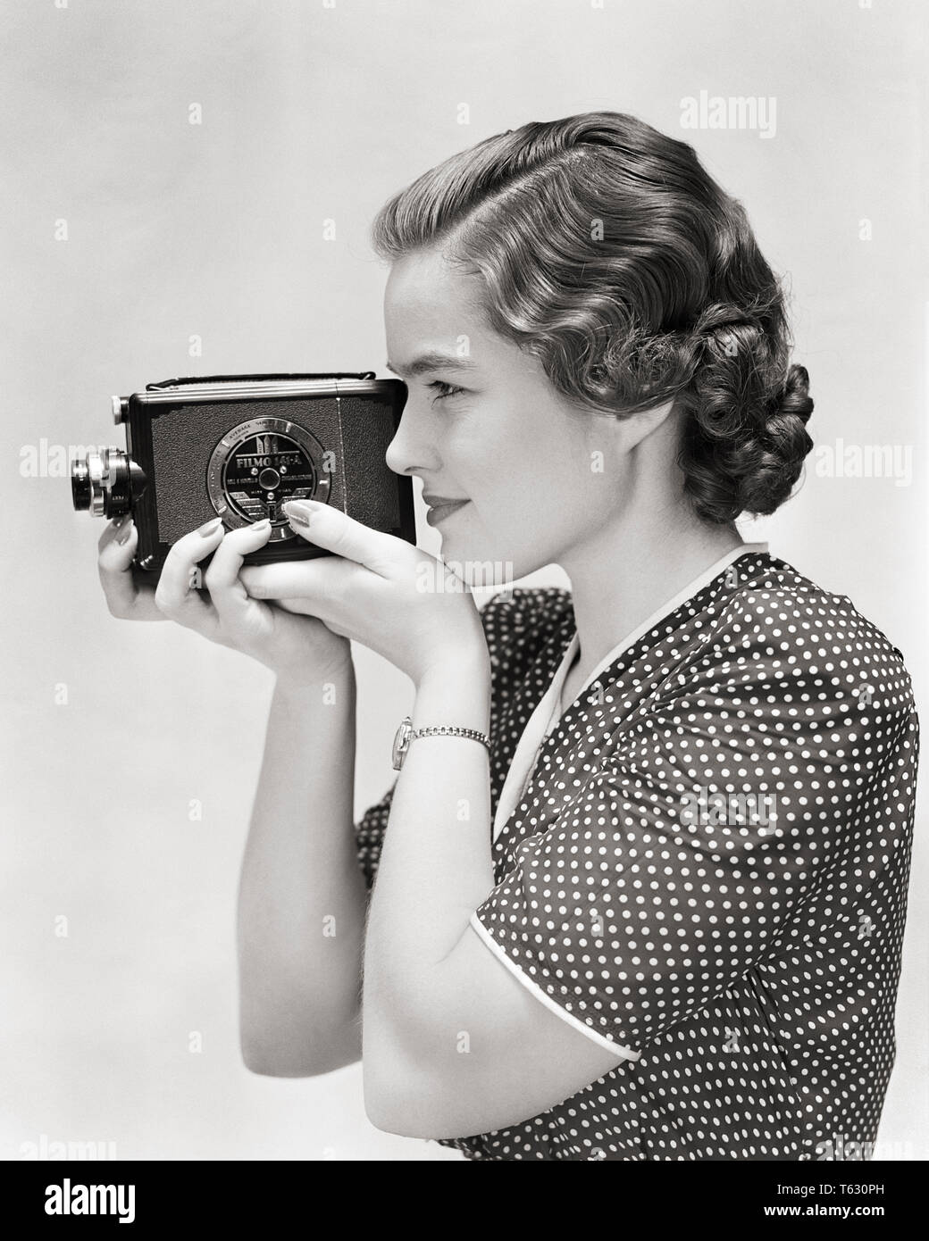 1930 Profilo della giovane donna usando un 8MM HOME MOVIE CAMERA - u399 HAR001 REGISTRAZIONE HARS B&W specialità in attività di scoperta di divertimenti HOBBY INTERESSE PER IL TEMPO LIBERO gli hobby conoscenza passatempo ricreazione a fotografare il piacere di opportunità utilizzando elegante concettuale 8MM creatività relax giovane donna adulta AMATORIALE IN BIANCO E NERO di etnia caucasica GODIMENTO HAR001 in vecchio stile Foto Stock