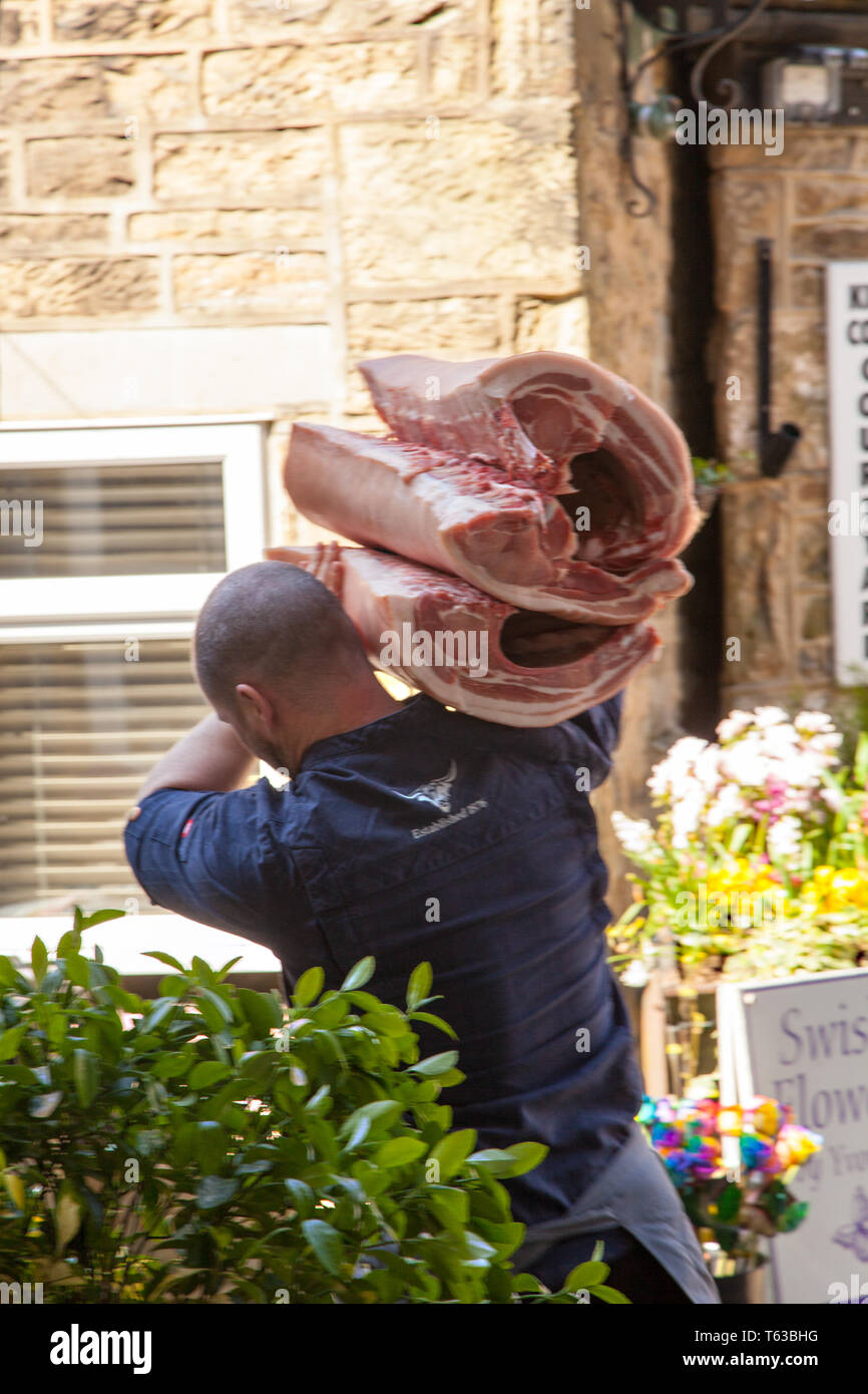 Uomo che porta i giunti di carne sulla sua spalla garantendo la carne ad un negozio di macellaio Foto Stock