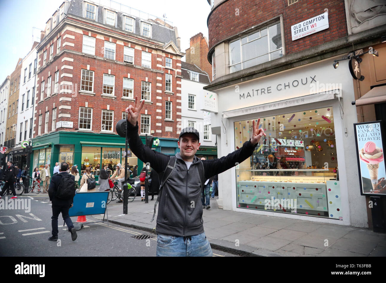 Giovane uomo felice sollevando entrambe le braccia e facendo segno di vittoria in Little Italy, SOHO, London, England, Regno Unito Foto Stock