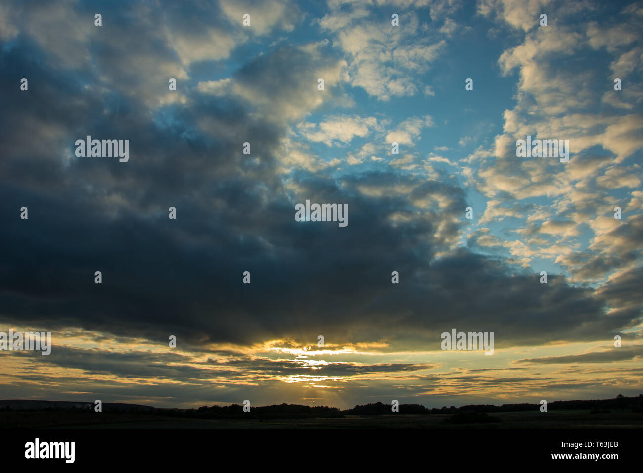 Il piercing al tramonto attraverso la serata grigio nuvole nel cielo blu, skyline e alberi Foto Stock