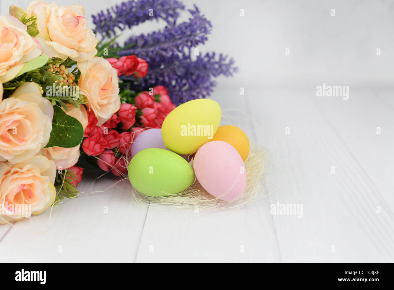Pasqua uova dipinte con un nido e fiori di rose su un bianco sullo sfondo di legno per le vacanze Foto Stock